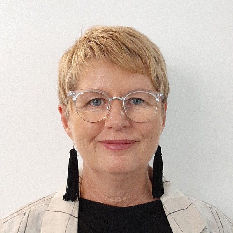 A woman smiling with short hair, glasses and dangly, fringe earrings.