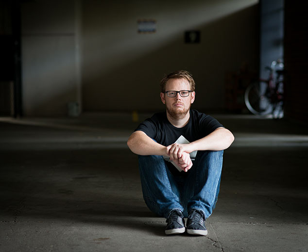 A picture of a man sitting on the concrete floor, wearing jeans and a t-shirt.