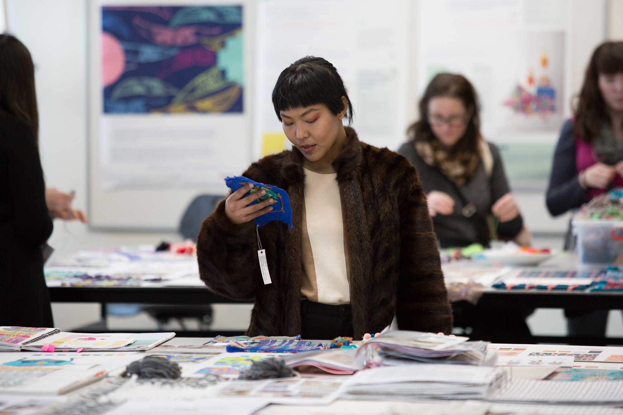 A woman wearing a fur jacket looking at fabric swatches.