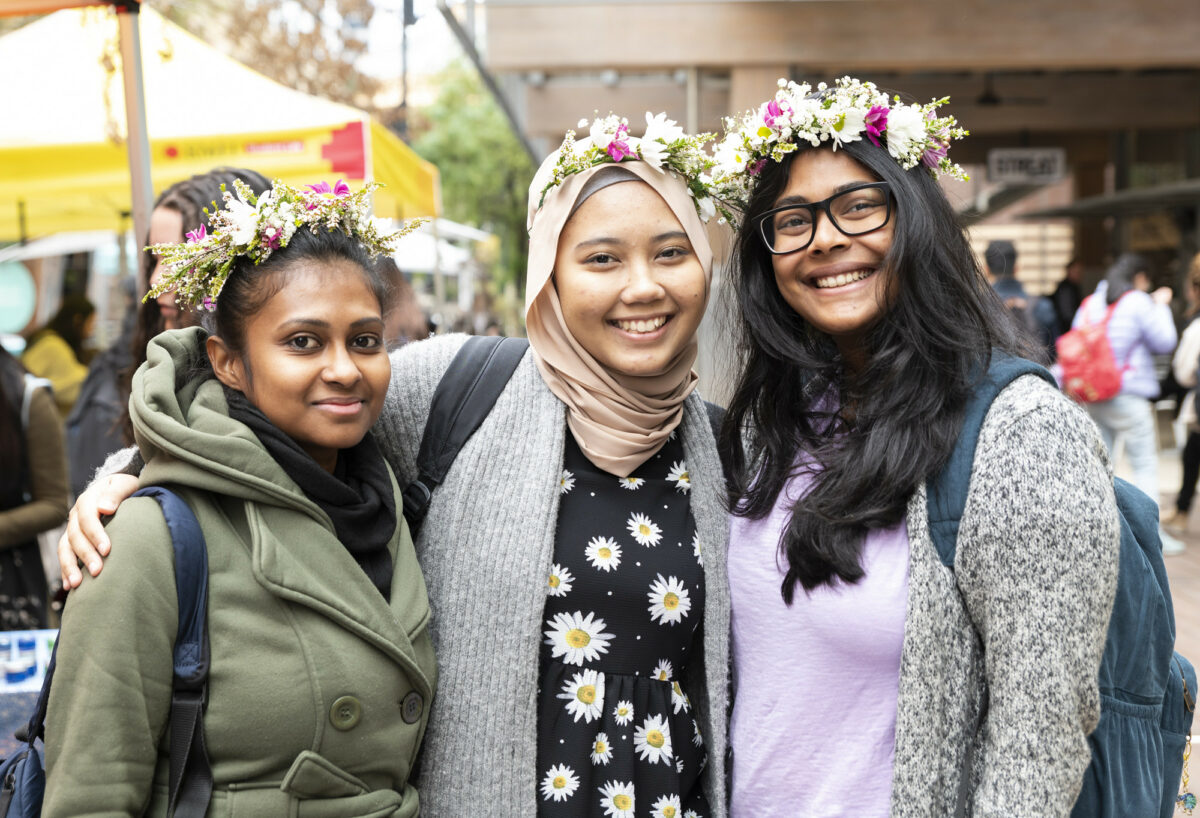 Three smiling international students wearing flower crowns.