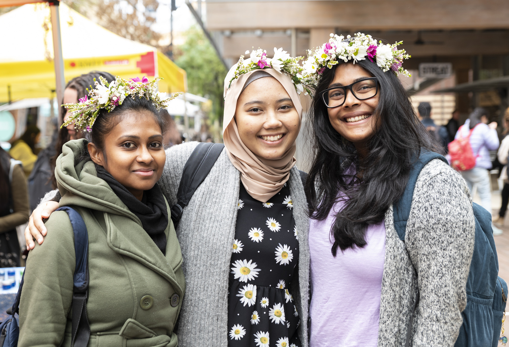 Three smiling international students wearing flower crowns.