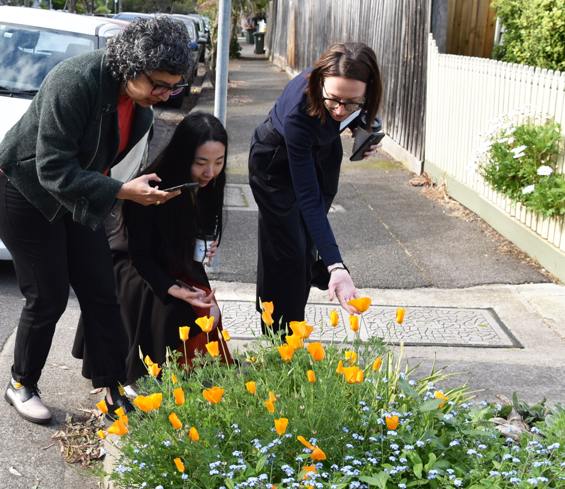 Three women crouching down to look at a garden bed.