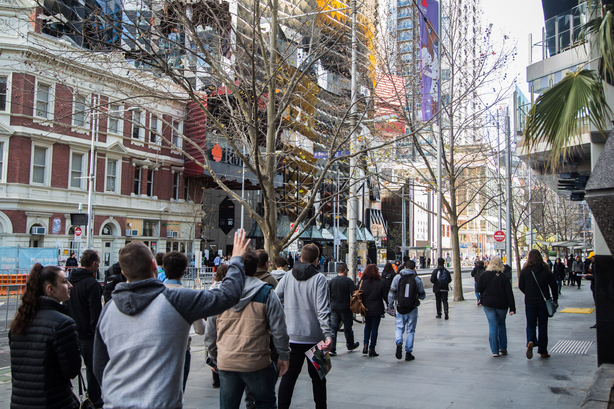 A group of people walk along Swanston street in the Melbourne CBD. RMIT is featured in the background