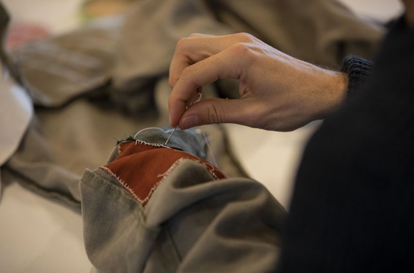 A hand mending a garment with a needle.