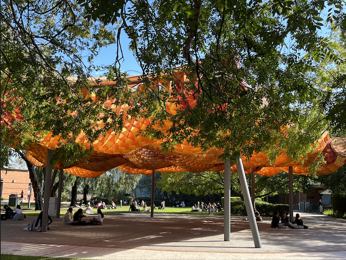 Trees surrounding an orange outdoor shelter with people sitting underneath.
