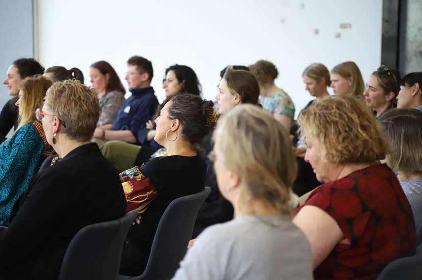 People seated in a room, listening and watching.